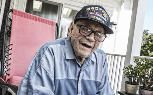 A 93 year old United States Army World War II and Korean Conflict US Air Force military veteran at home relaxing on his front porch. He's wearing a common, unbranded, generic souvenir shop military veteran commemorative baseball style cap.