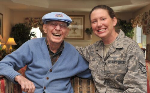 An older veteran with a younger veteran. Both are smiling.