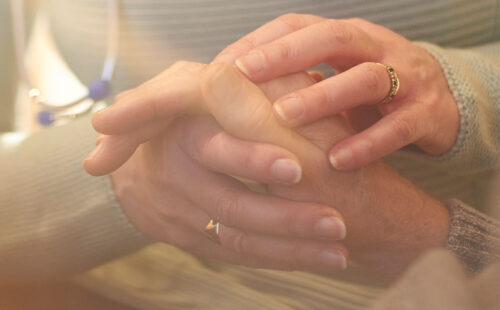 Older caregiver holding hand of elderly patient.