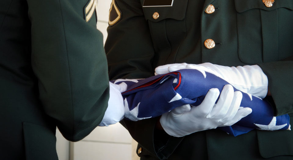 A soldier presents another soldier with a folded US flag