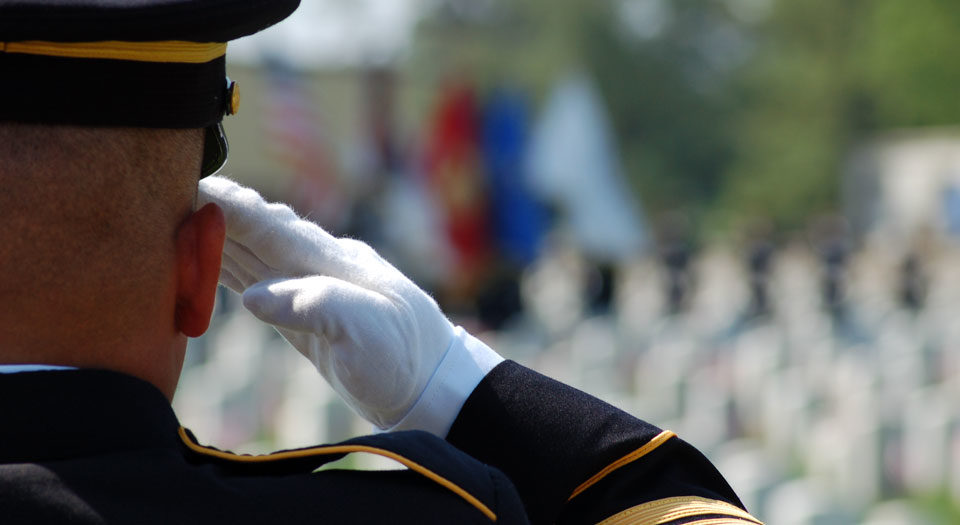 Solider in dress uniform saluting graves. His back is to us.