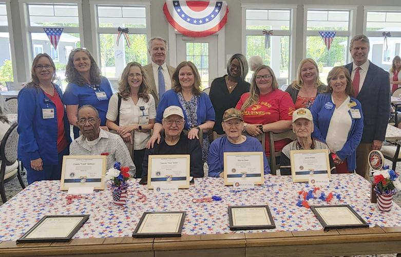 A group of veterans sit at table. Certificates are in front of them. Behind them are various hospice staff members and volunteers.