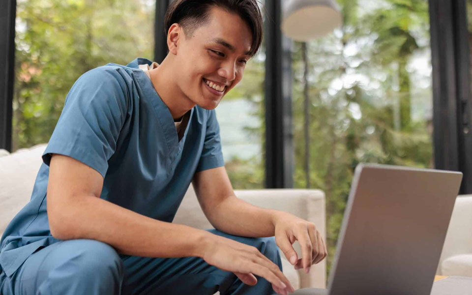 A person in scrubs is sitting at a laptop. They are engaged with whatever they are watching.